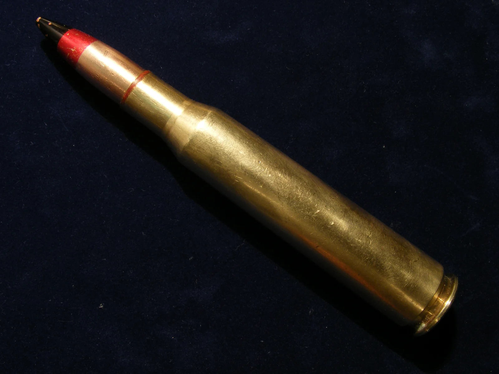 A large brass bottleneck cartridge with a red-tipped bullet, standing against a dark background