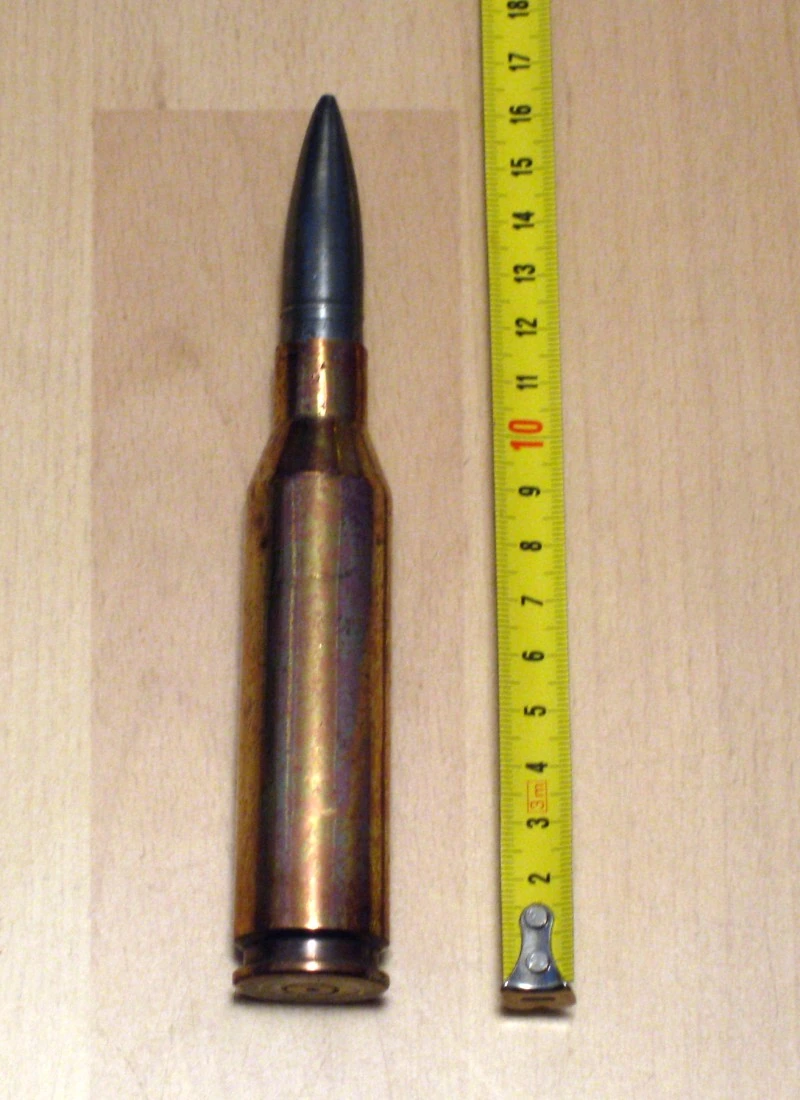 A single large brass bottleneck cartridge with a dark pointed bullet, measured against a tape rule