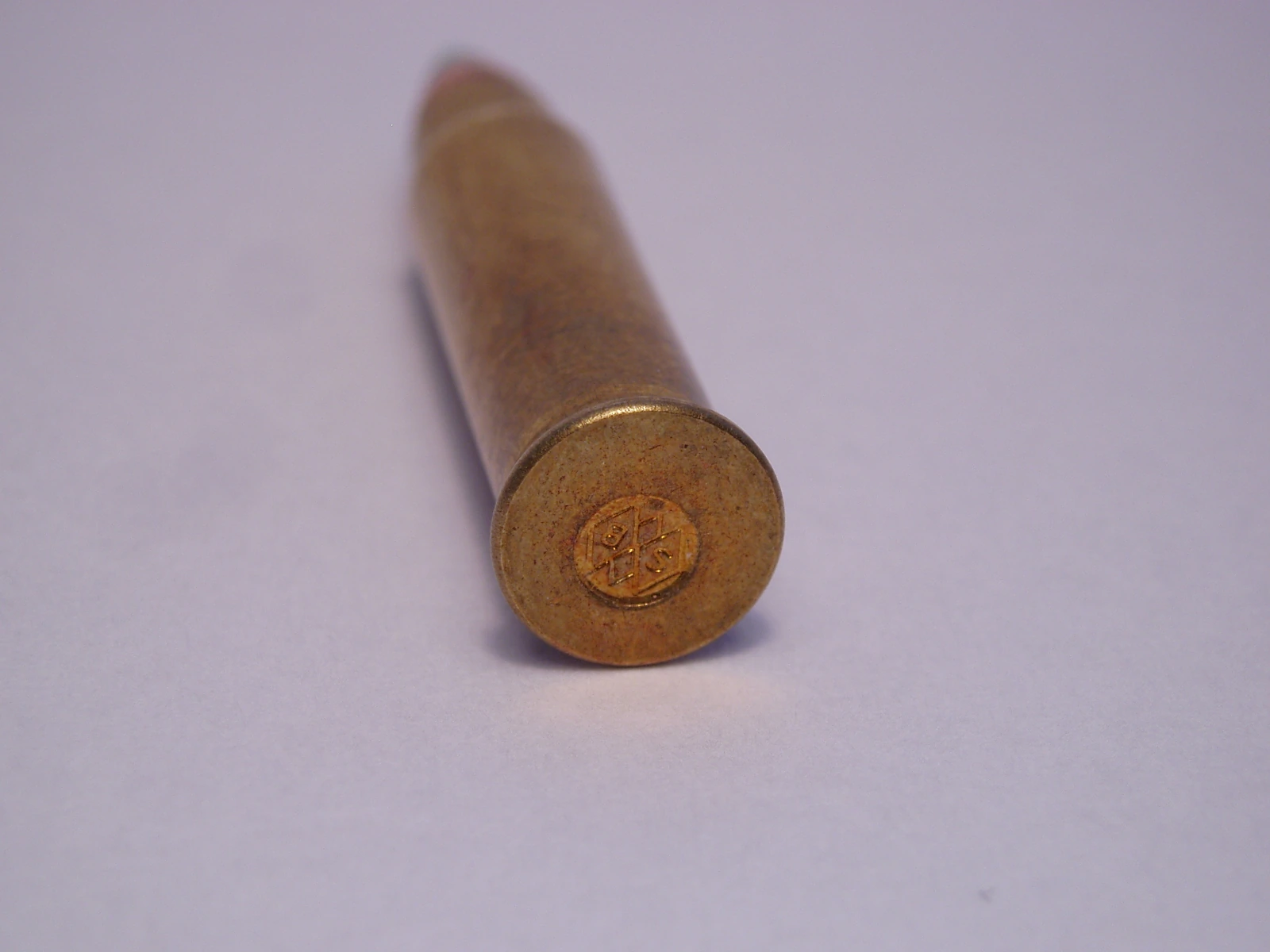 A close-up of a small rimfire cartridge's brass base, stamped with a Sellier & Bellot headstamp, with a slender pointed bullet with a coloured tip receding out of focus.