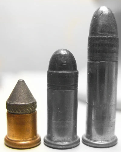 Three rimfire cartridges of increasing size standing upright: a very short, wide-headed cartridge with a conical bullet almost as tall as its case on the left, a slightly taller round-nosed cartridge in the middle, and a longer one on the right.