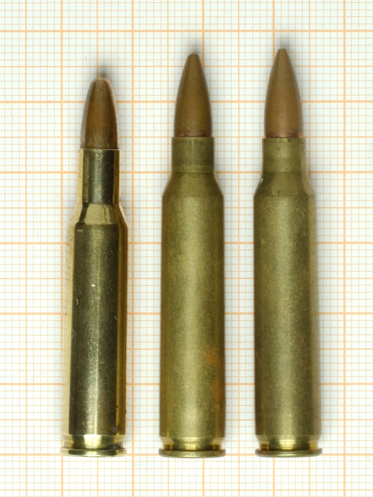 Three similar small-bore rifle cartridges of increasing case length standing on graph paper: .222 Remington, .223 Remington and 5.56x45mm NATO