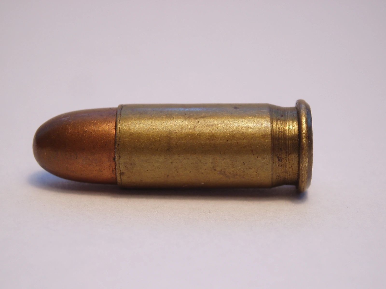 A .25 ACP pistol cartridge lying on its side, a small round-nose full metal jacket bullet seated in a short brass semi-rimmed case.