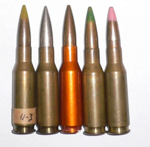 Five .280 British ball cartridges standing in a row, one with an orange-coloured aluminium case among the usual brass ones.