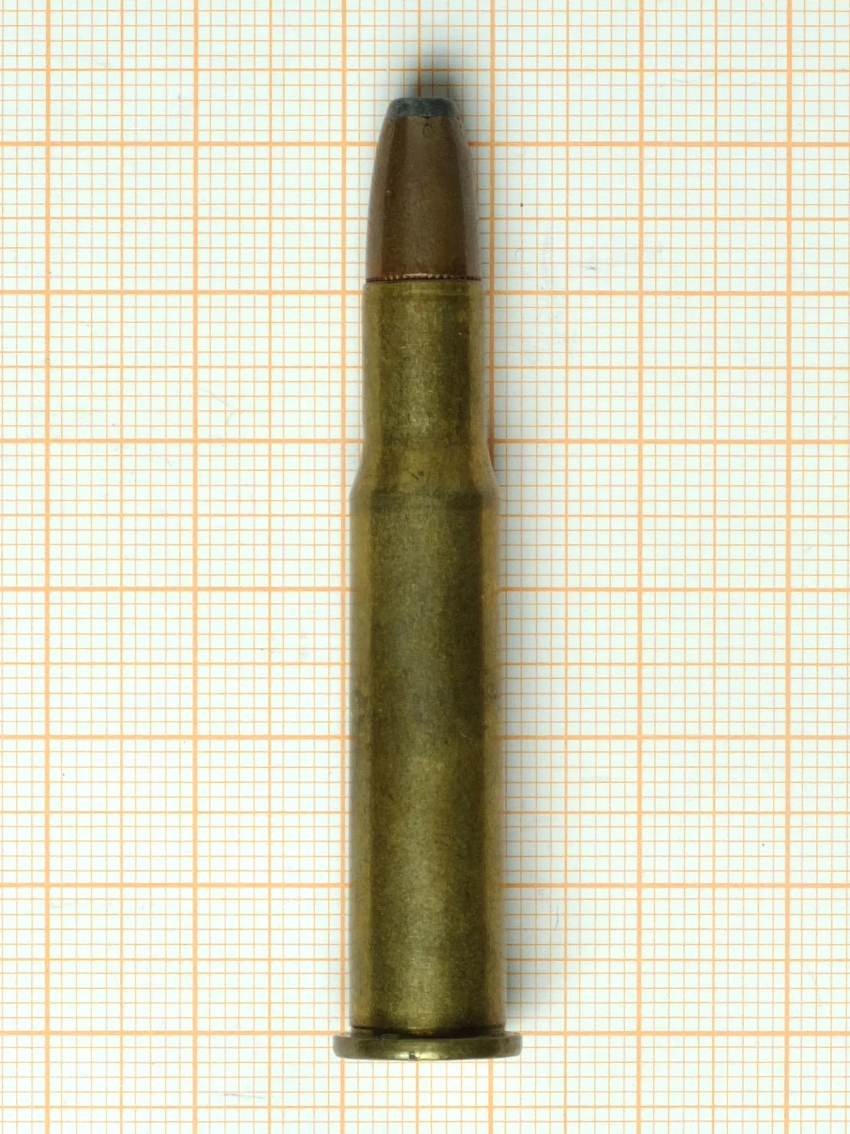 A single .30-30 Winchester cartridge on graph paper: a rimmed, gently tapered brass case topped with a flat-tipped soft-point bullet