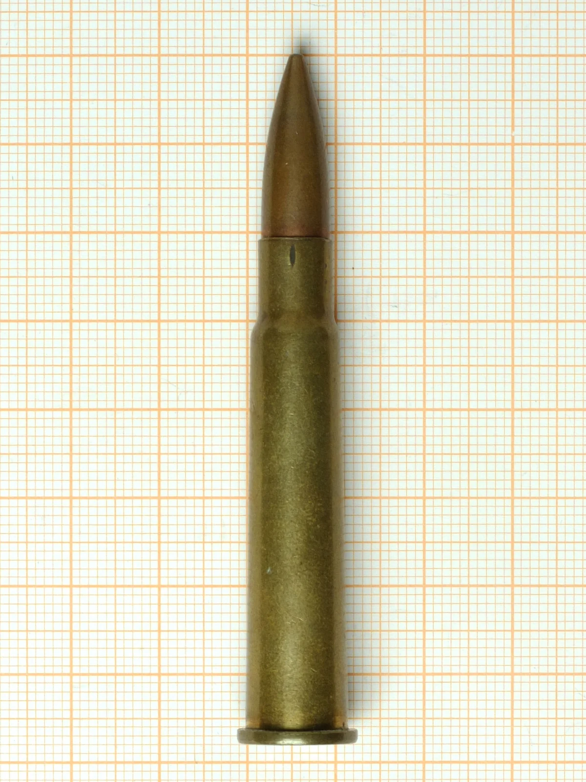 A .303 British cartridge lying on orange graph paper, its rimmed base clearly wider than the case body.