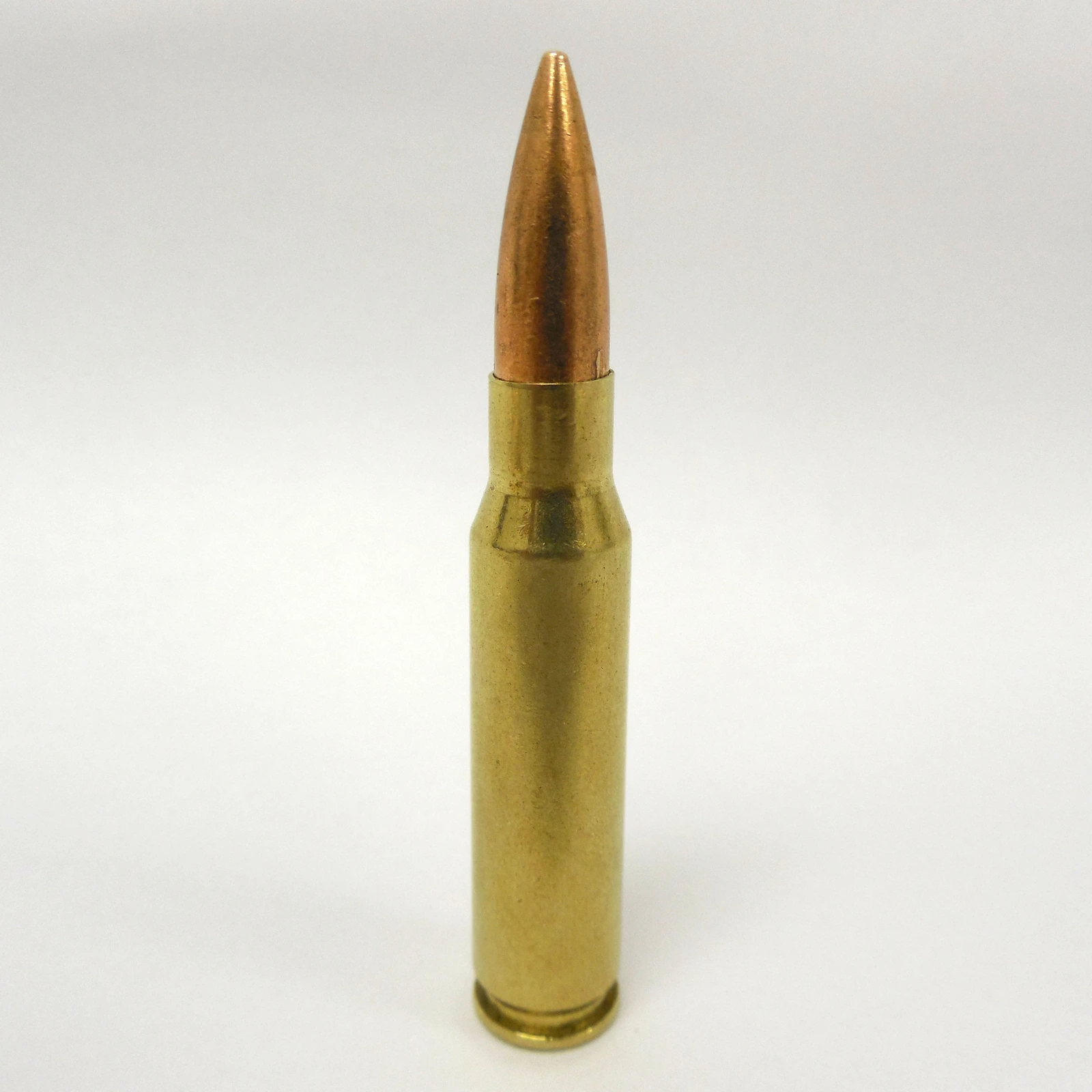 A .308 Winchester cartridge standing upright on a plain grey ground, lit from the side.