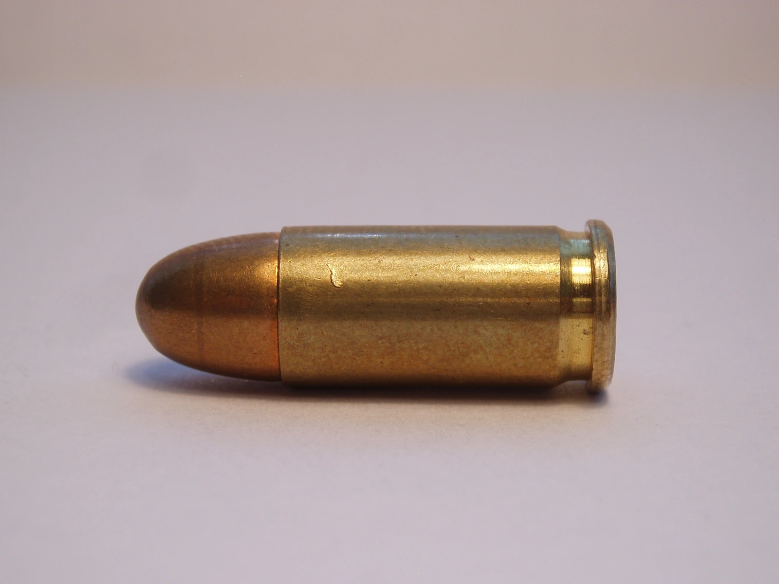 A .32 ACP pistol cartridge lying on its side, a round-nose full metal jacket bullet seated in a brass semi-rimmed case with a small extractor groove.