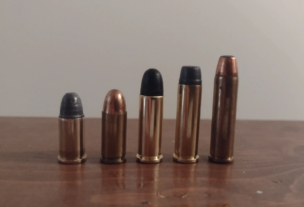 Five .32-caliber handgun cartridges of increasing length standing in a row on a wooden surface