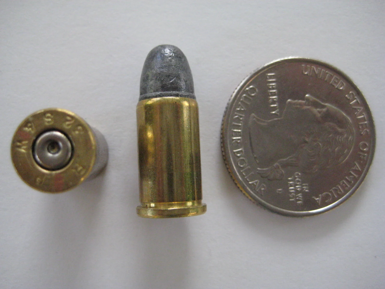 A loaded .32 S&W cartridge and an empty brass case with its headstamp visible, beside a coin for scale