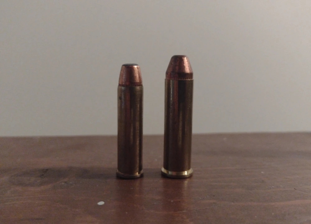 Two brass rimmed revolver cartridges standing side by side, the right one visibly longer