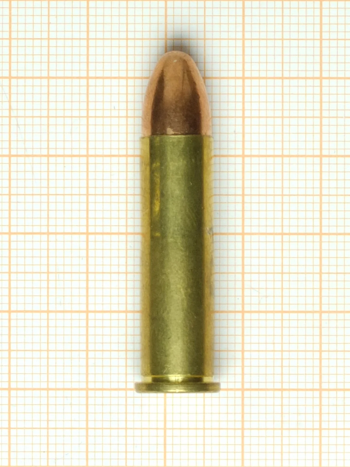 A .357 Magnum cartridge on orange graph paper, its straight case ending in a narrow rim.