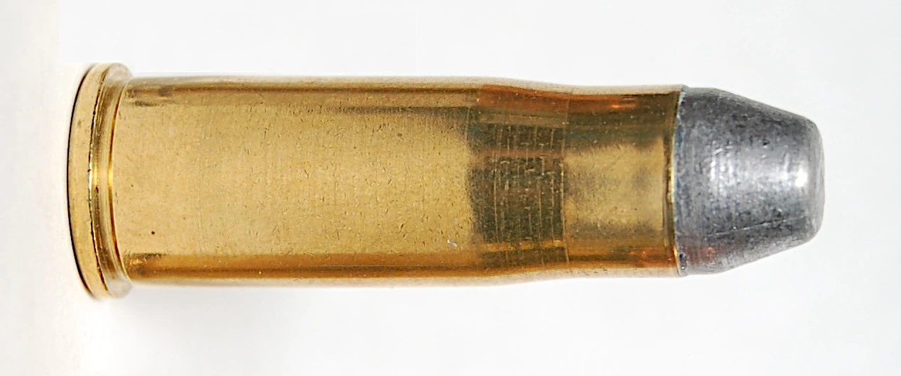 A single rimmed, bottlenecked brass cartridge lying on its side against a pale ground, with a rounded lead bullet visible at its mouth.