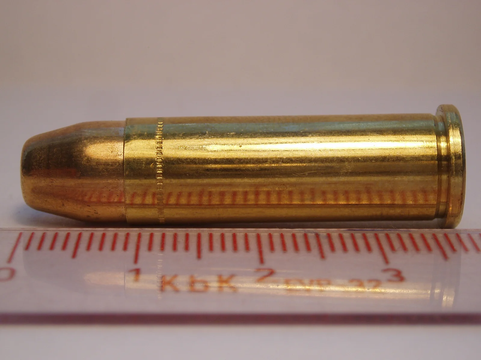 A .38 Special cartridge lying on its side across a ruler, the hollow point in its bullet visible at the tip.
