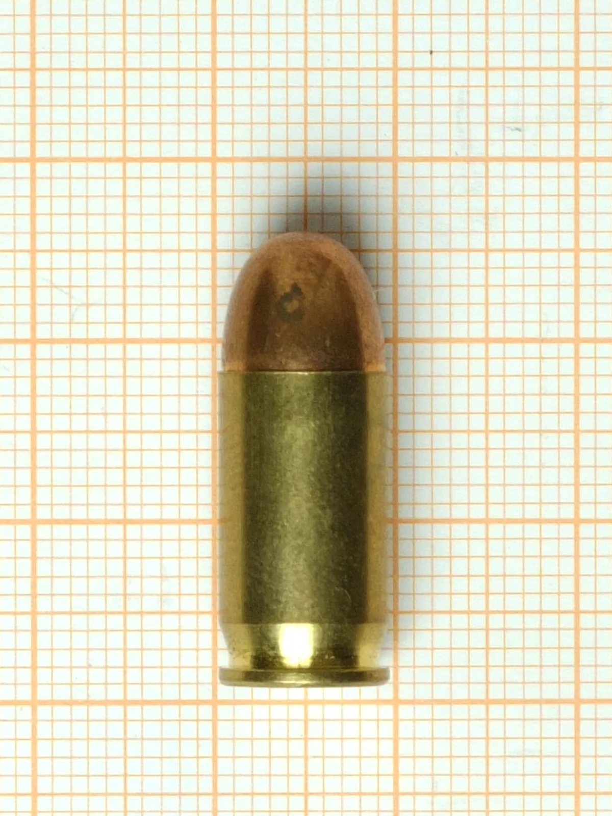 A .380 ACP cartridge on orange graph paper, short and straight-walled with a rounded jacketed bullet.