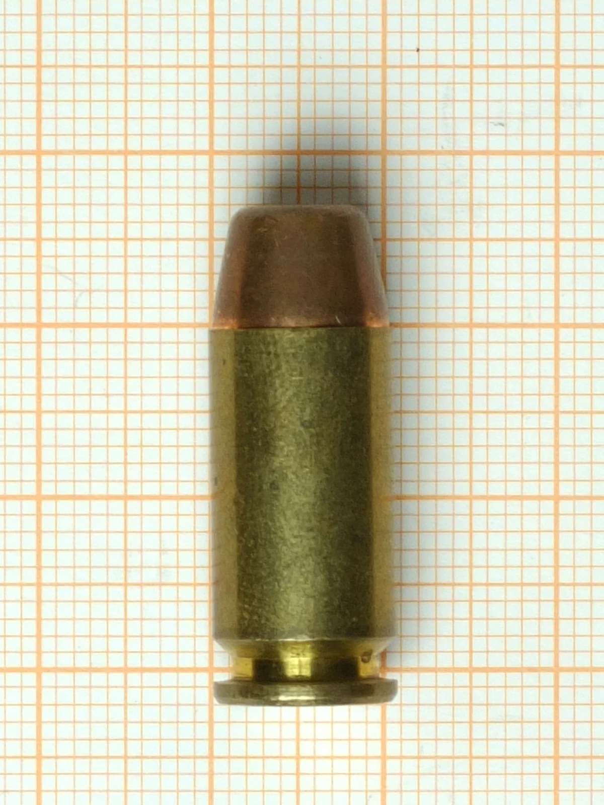 A .40 S&W cartridge on orange graph paper, straight-walled with a rounded jacketed bullet.