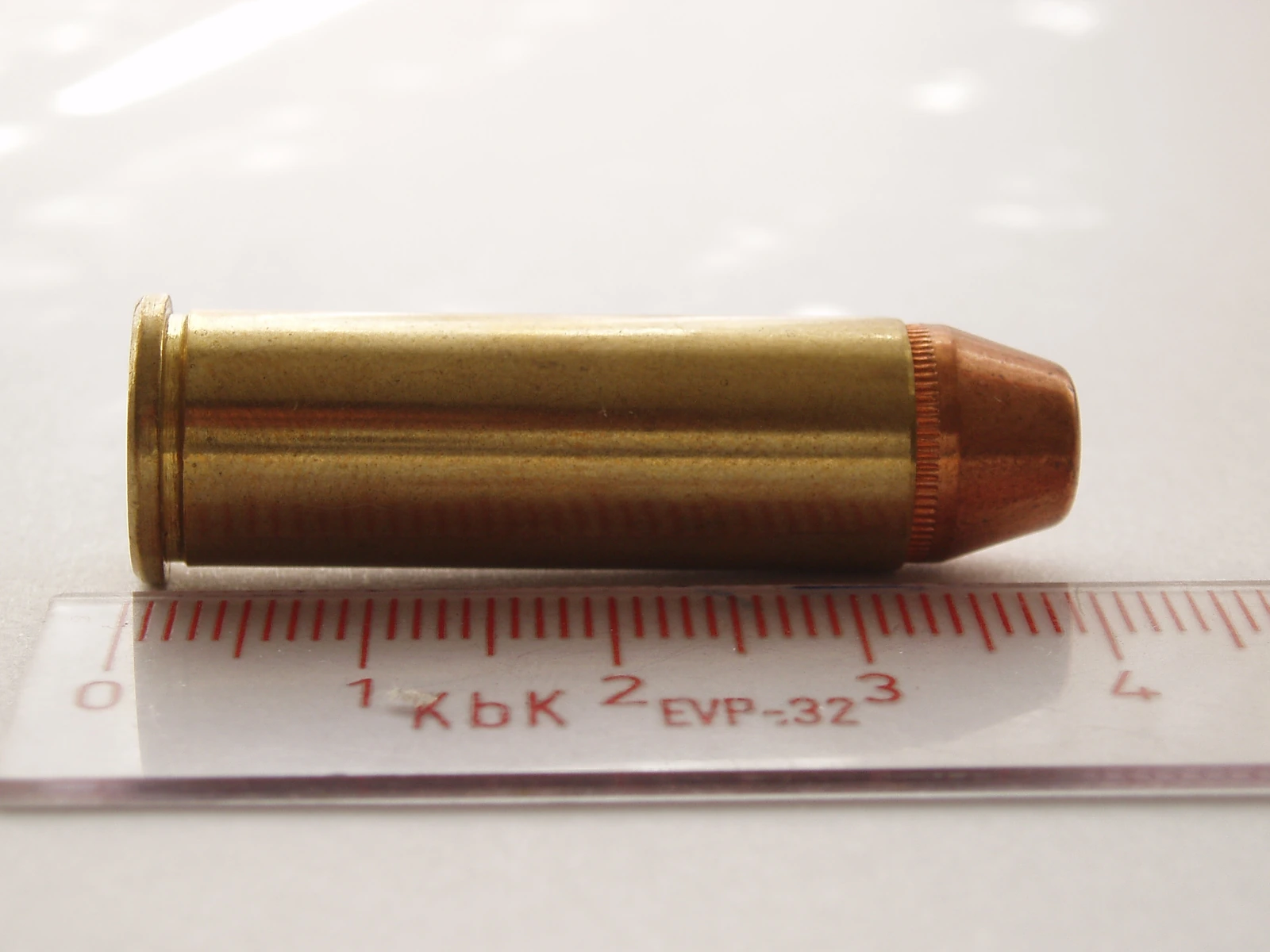 A rimmed revolver cartridge with a brass case and a soft-point bullet, lying on a millimetre ruler that measures it at roughly 41 mm overall.