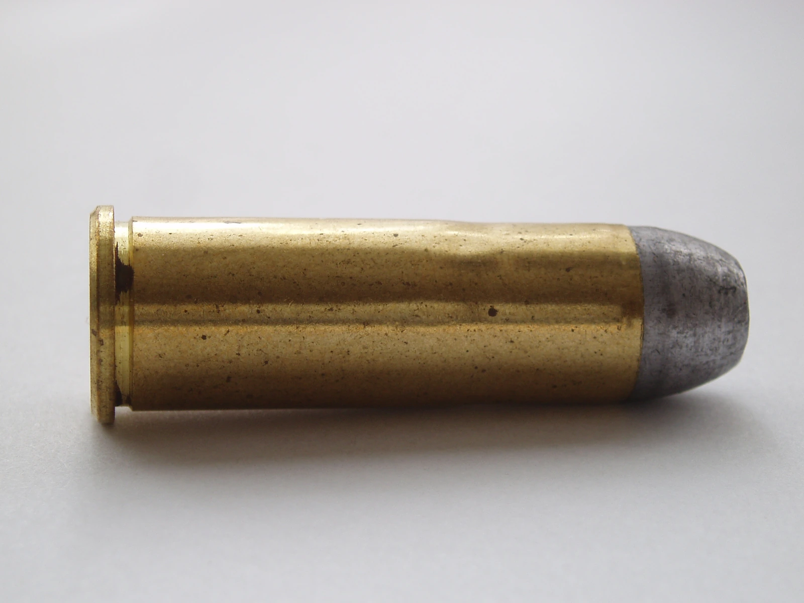 A .44-40 Winchester cartridge lying on its side on a pale ground, carrying an unjacketed lead round-nose bullet.