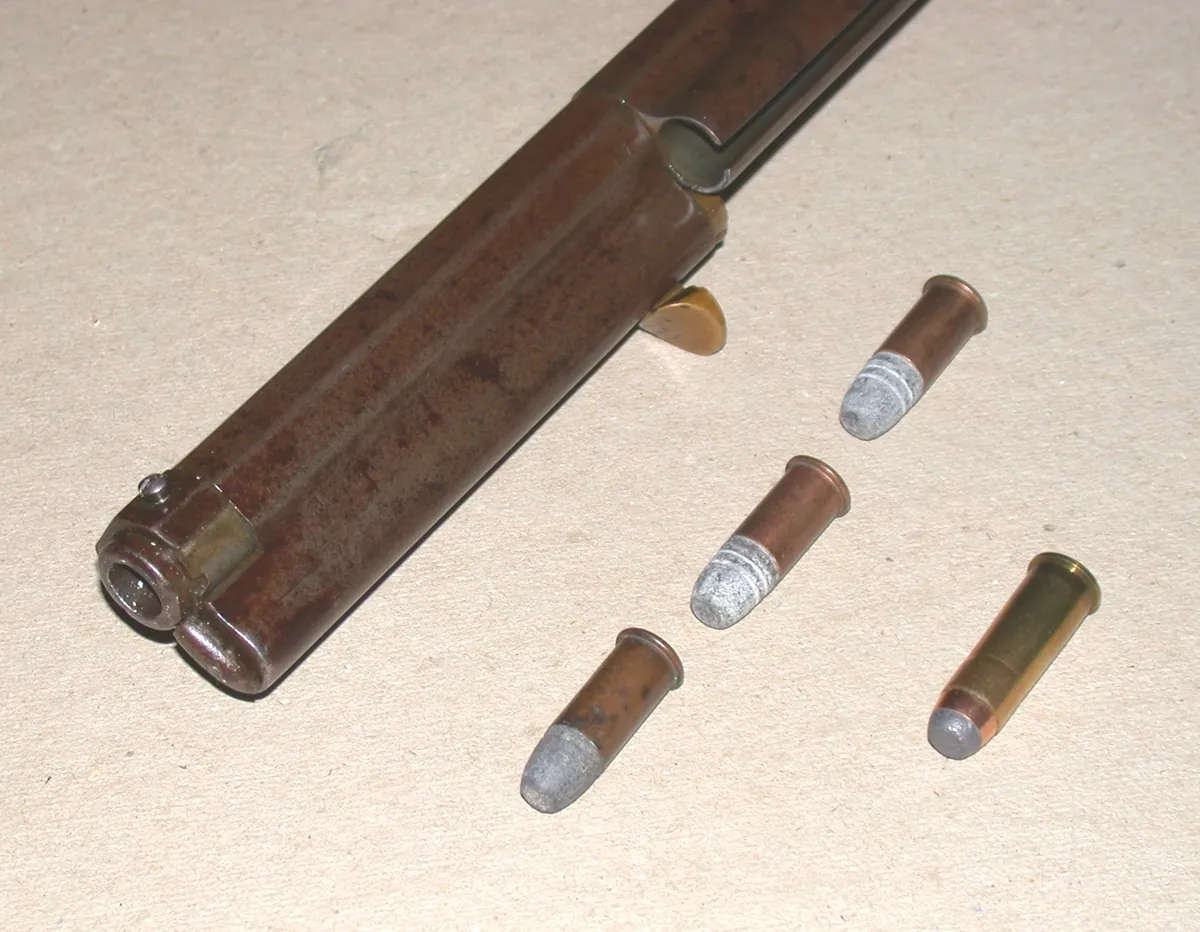A Henry rifle's open tubular magazine beside loose .44 Henry cartridges and a .44-40 round for comparison