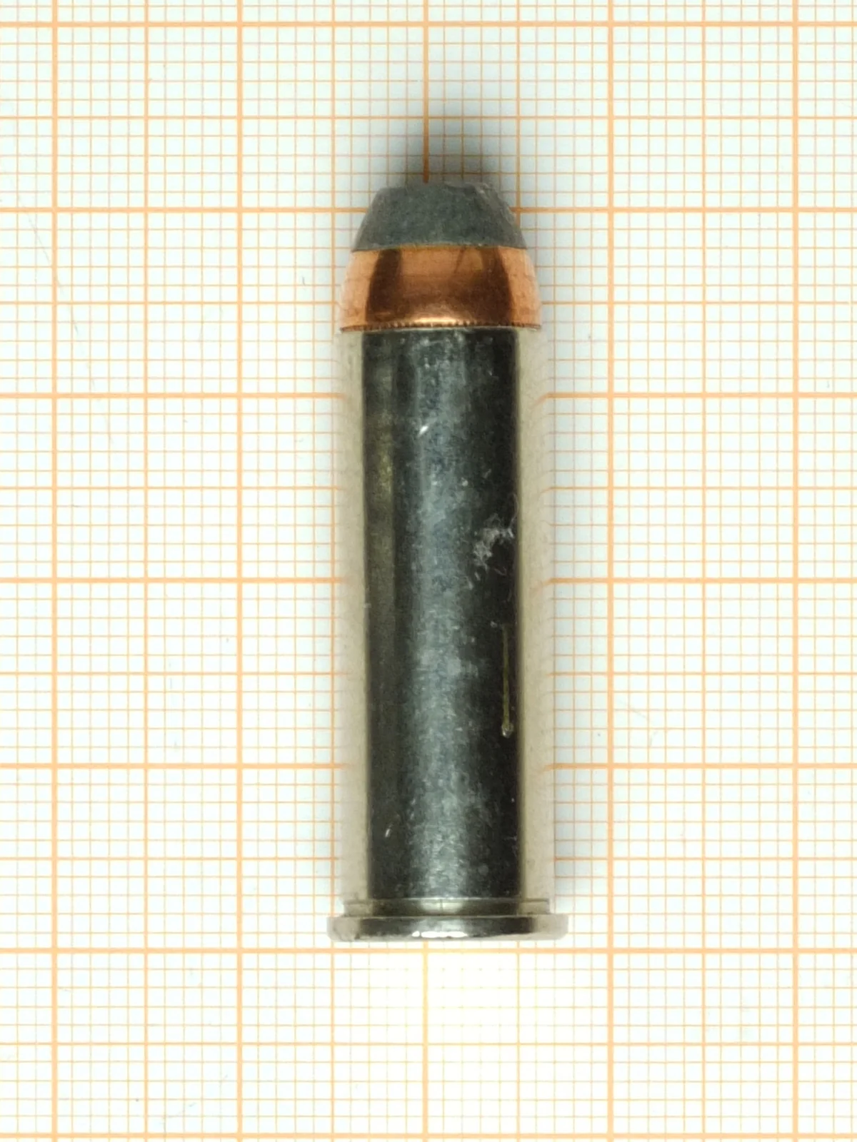 A .44 Magnum cartridge on orange graph paper, its case dark with age and its bullet flat-nosed.