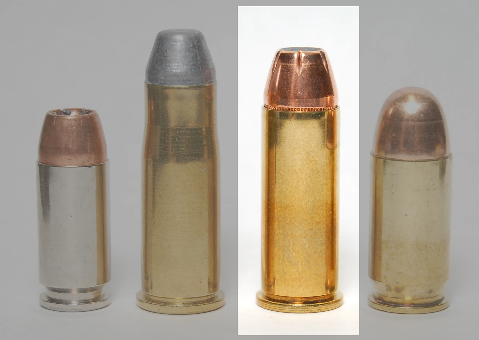 Four handgun cartridges standing upright, side by side; a .44 Special round, second from the right with a jacketed hollow-point bullet, is set off against a white background while the other three sit on grey.