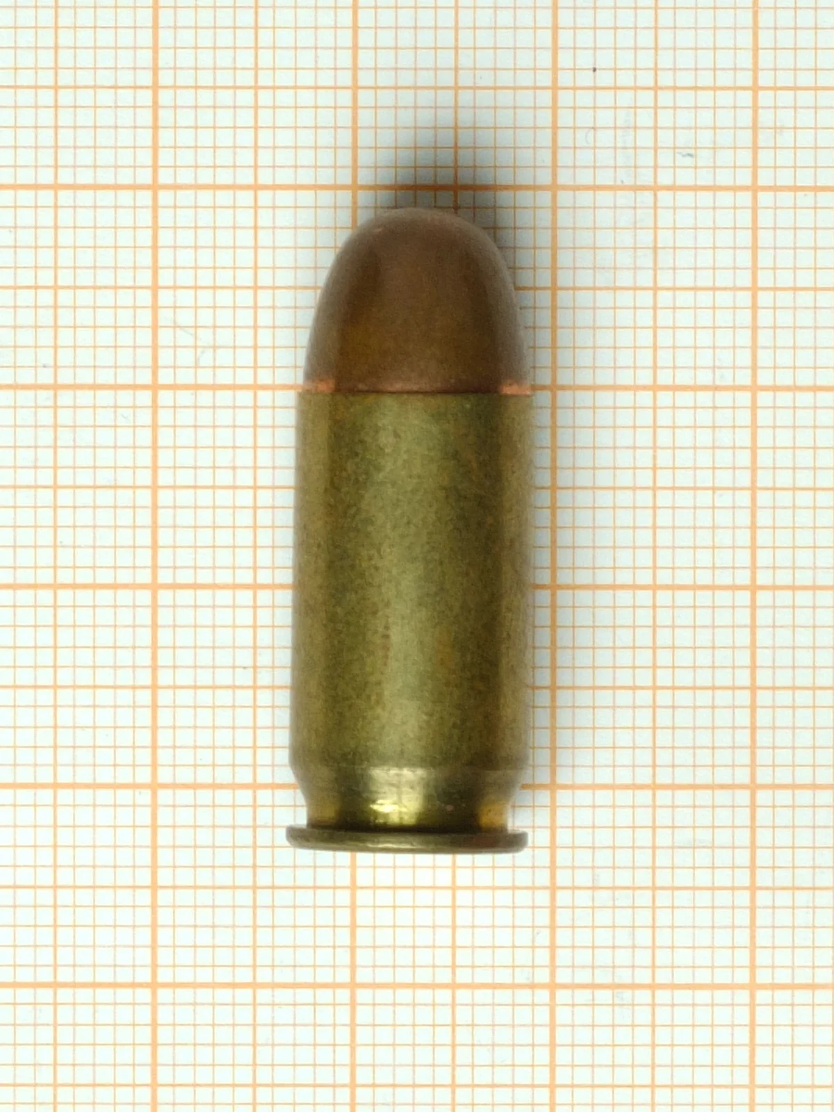 A .45 ACP cartridge on orange graph paper, short and wide with a rounded full metal jacket bullet.