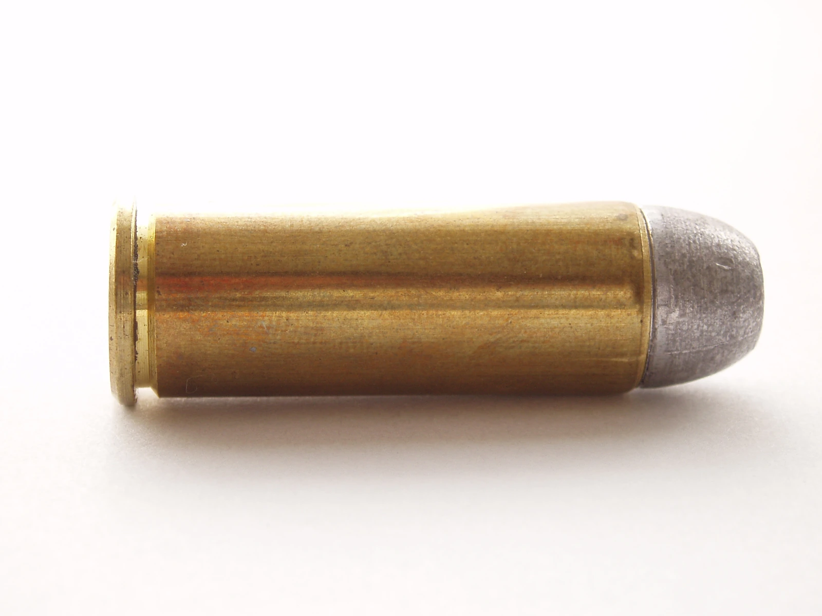 A .45 Colt cartridge lying on its side on a white ground, its long straight case ending in a blunt lead bullet.