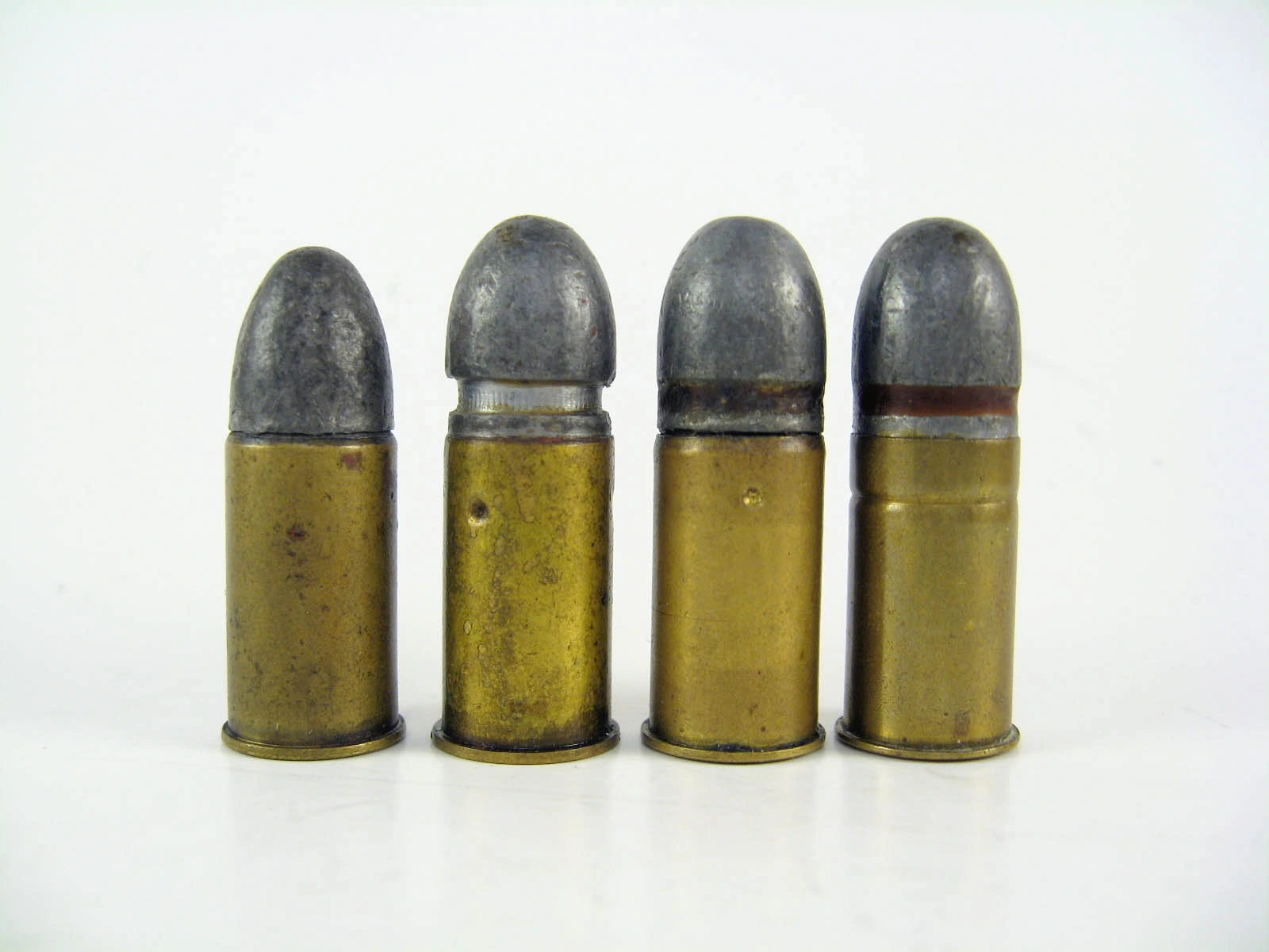 Four rimmed revolver cartridges with brass cases and lead round-nose bullets, standing upright side by side; the leftmost is slightly shorter than the other three.