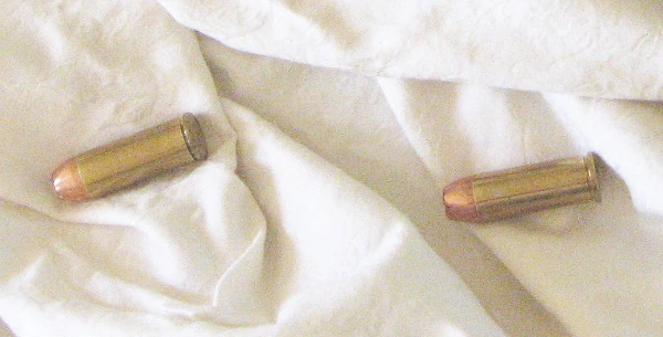Two short, wide brass revolver cartridges with copper-coloured bullets lying on a crumpled white cloth.