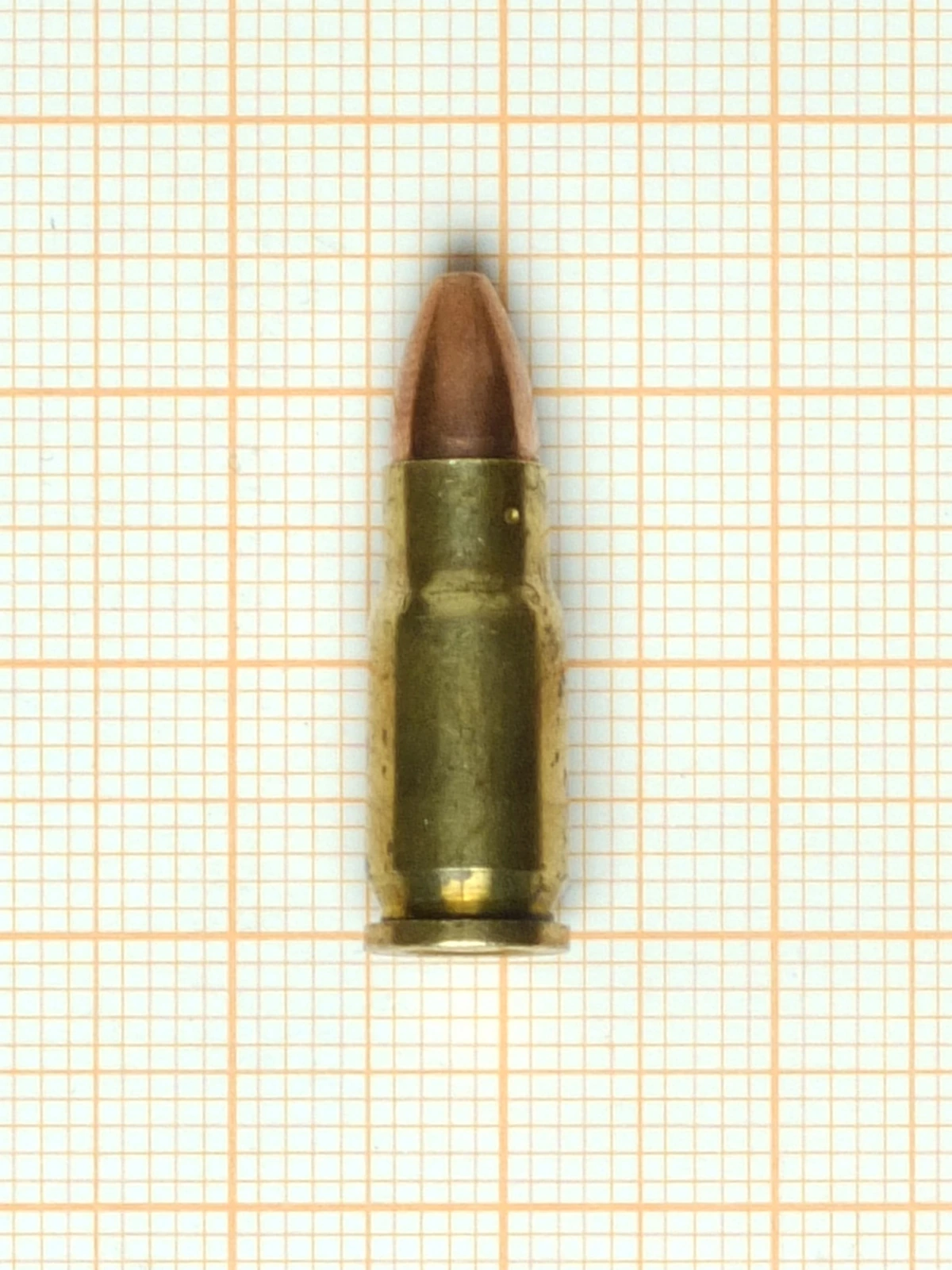 A small rimless bottleneck pistol cartridge with a rounded jacketed bullet, photographed on graph paper.