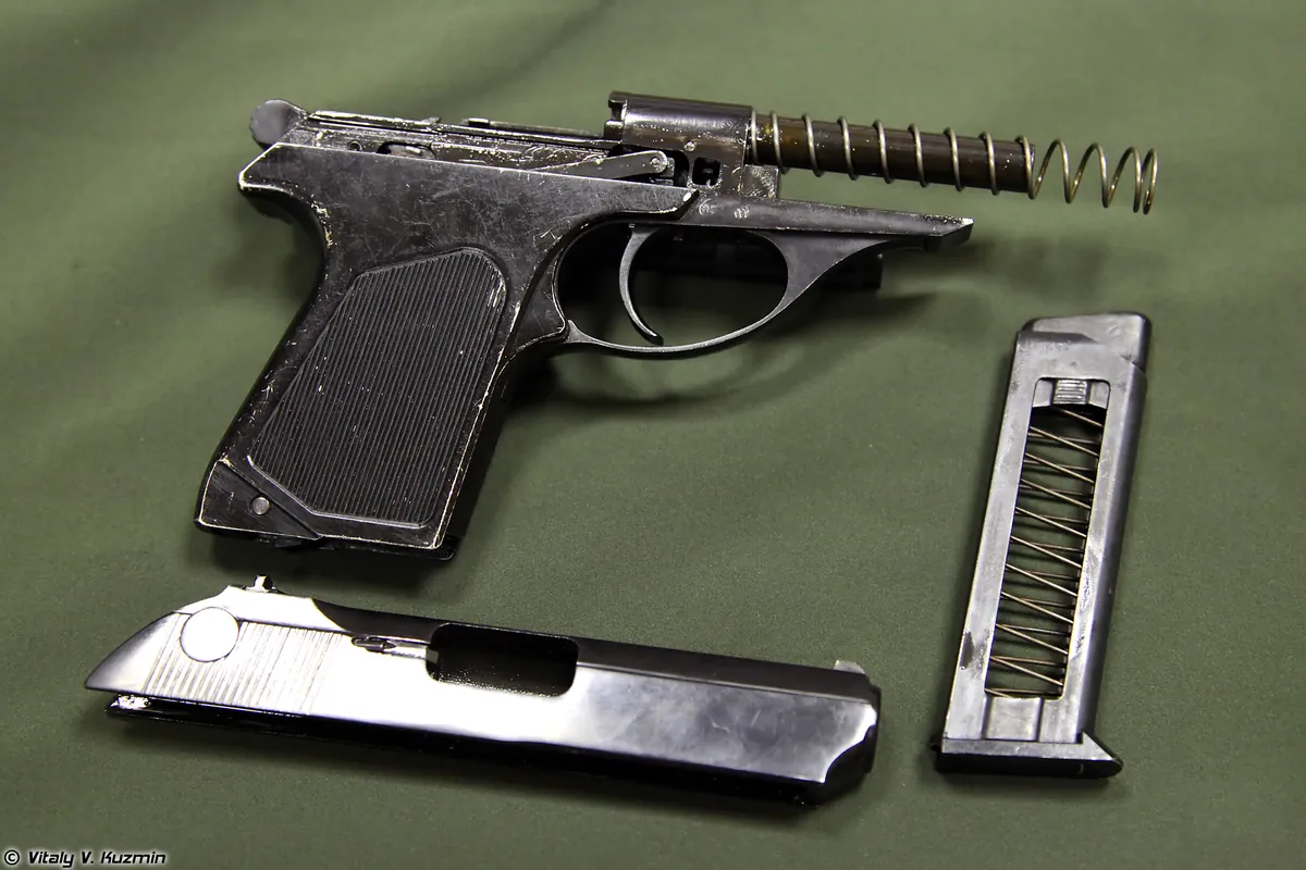 A small field-stripped pistol laid out in three parts — frame, slide and magazine — on a green cloth.