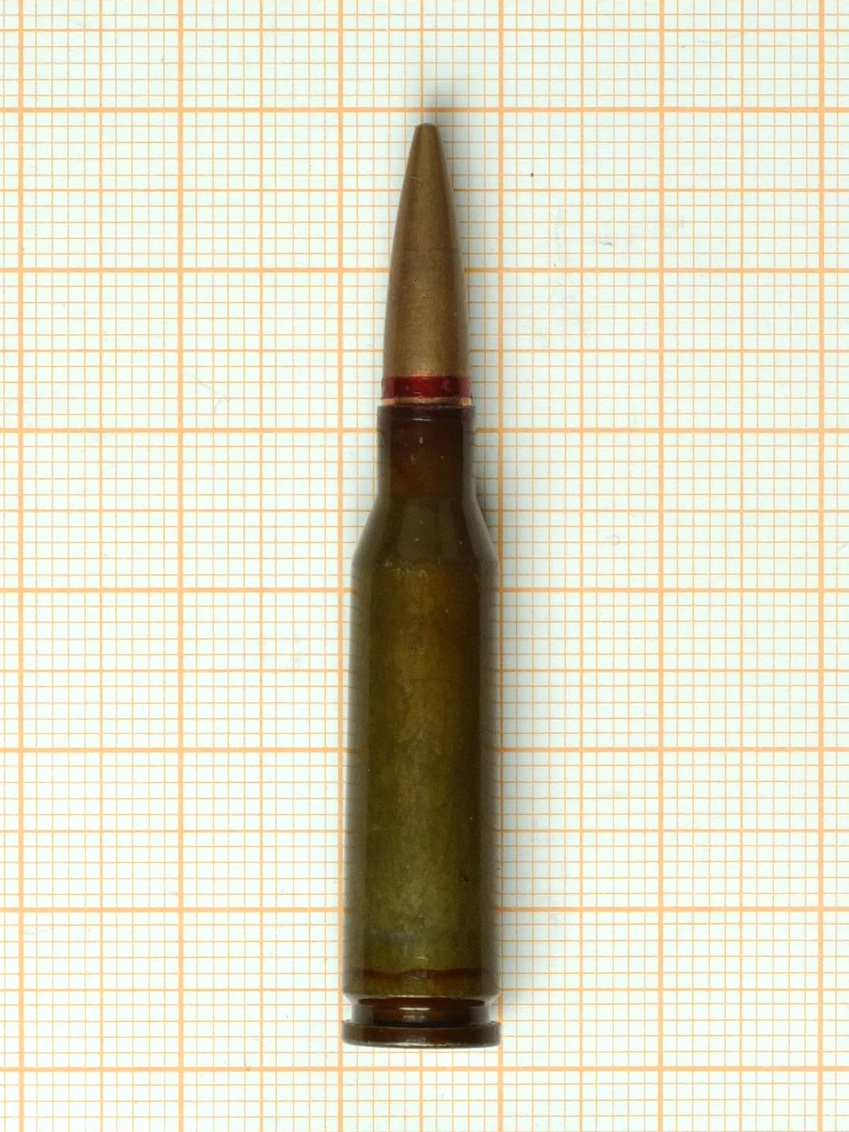 A 5.45×39mm cartridge on orange graph paper, sharply bottlenecked with a long pointed bullet and a red sealant band at the case mouth.