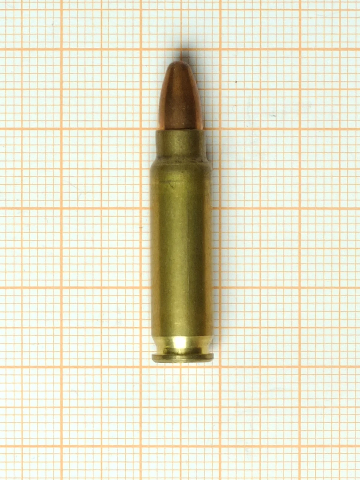A 5.7×28mm cartridge on orange graph paper, a small bottlenecked case with a short pointed bullet.