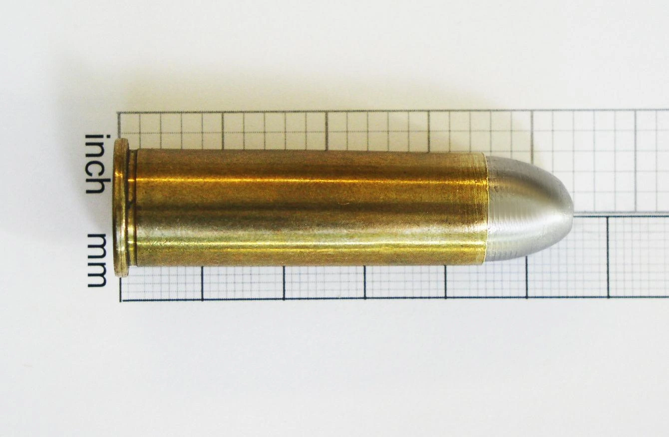 A single .50-70 Government cartridge with a brass case and a round-nosed lead bullet, lying on graph paper for scale