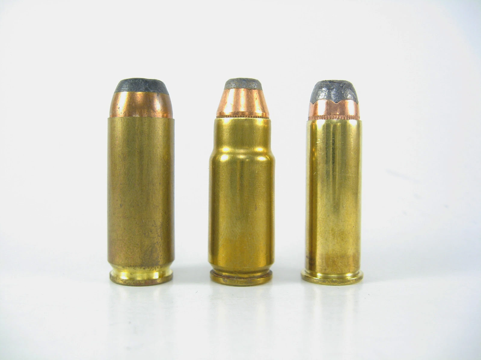 Three large-caliber pistol cartridges with brass cases and hollow-point bullets standing upright in a row