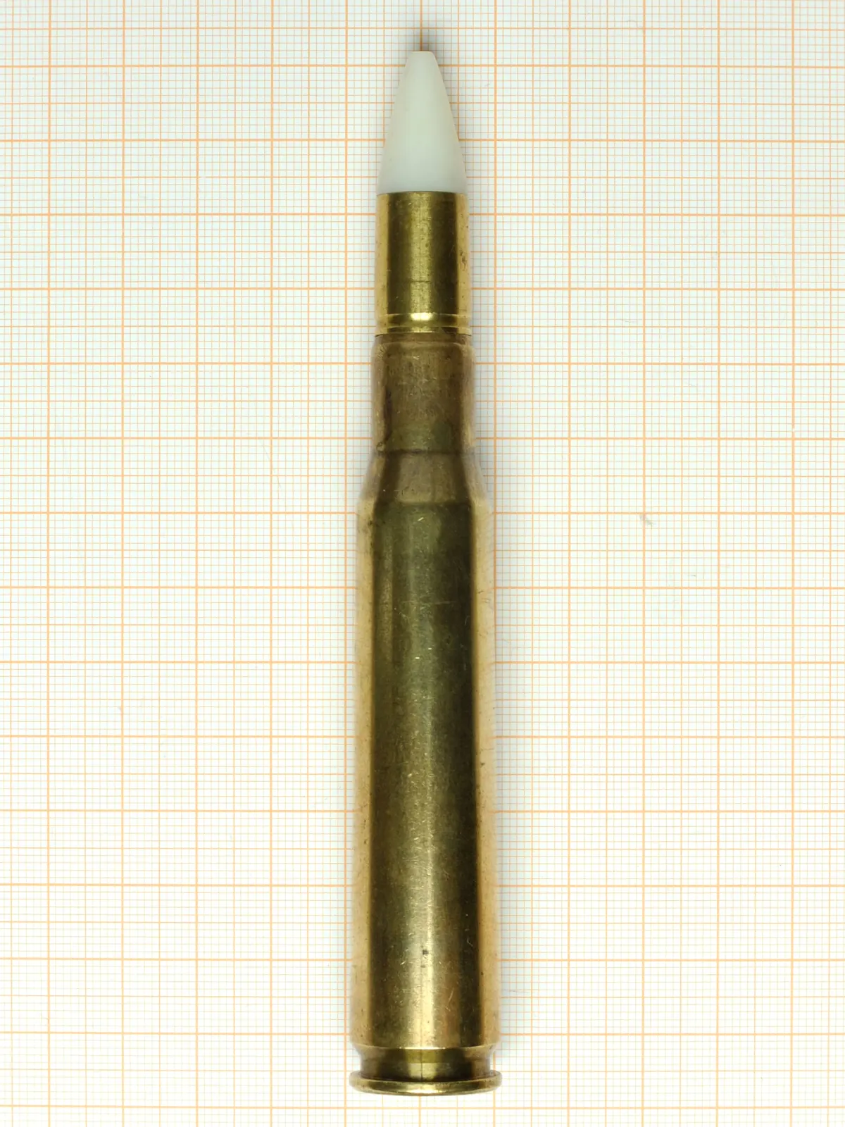 A .50 BMG cartridge on orange graph paper, a long bottlenecked case with a white-tipped bullet.