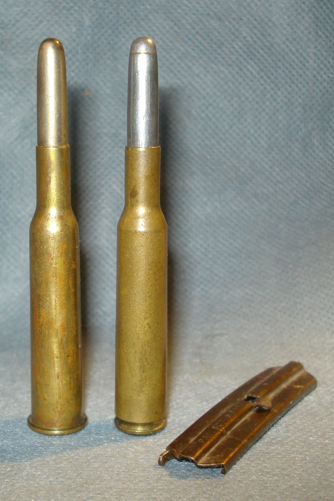 Two brass rifle cartridges of slightly different case profile standing beside a stripper clip.