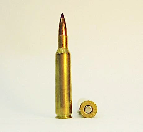 A single brass bottleneck rifle cartridge with a pointed copper jacketed bullet, standing beside its own base cap
