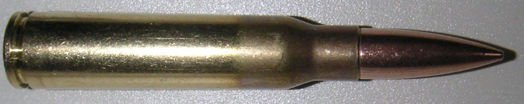 A 7.5×54mm French rifle cartridge lying on its side, a pointed spitzer bullet with a copper-coloured tip seated in a long brass bottlenecked case.