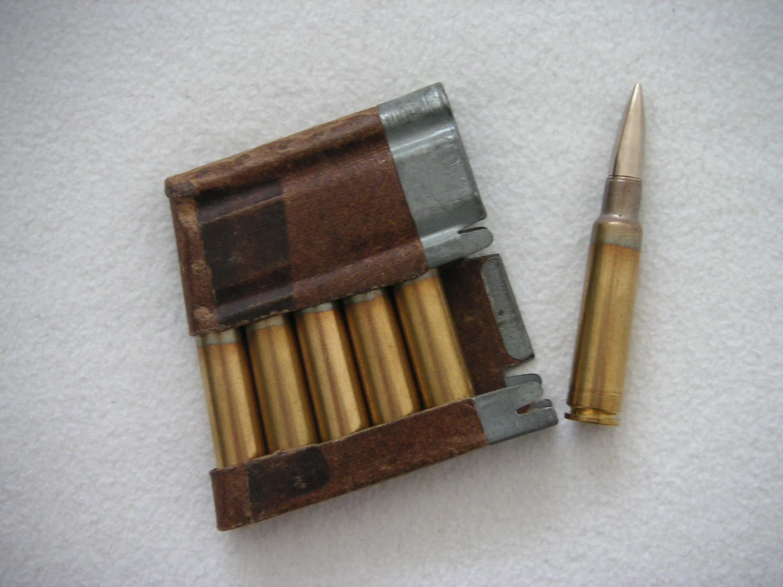 Six 7.5×55mm cartridges held in two metal charger clips, with a seventh loose round standing beside them.