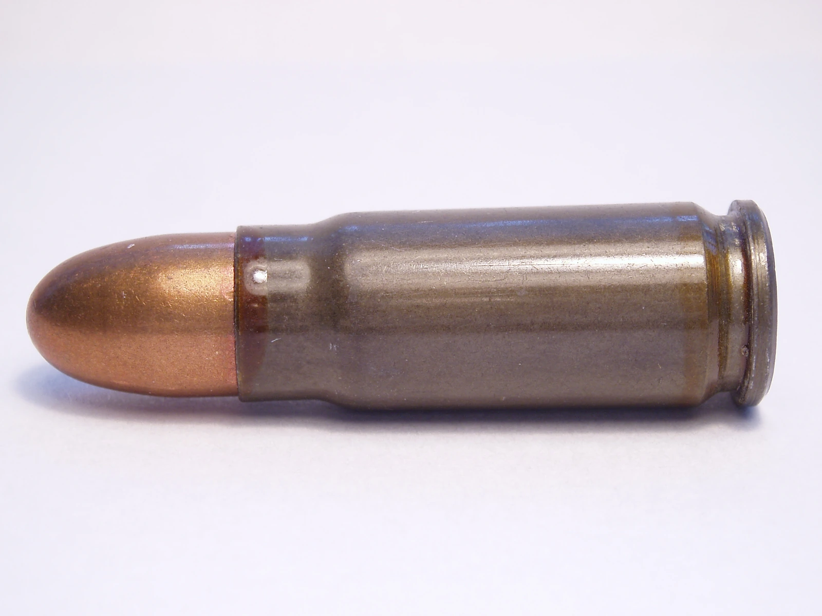 A 7.62×25mm Tokarev cartridge lying on its side, close up, its bottlenecked case bright and its bullet copper-jacketed.