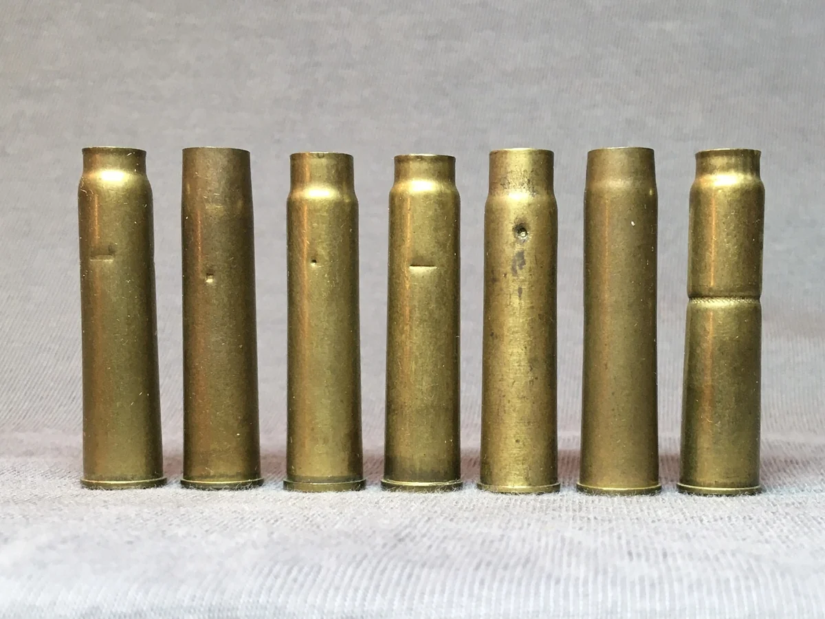 Seven brass 7.62×38mmR cases standing in a row, each showing a slightly different case-mouth crimp from a different commercial manufacturer