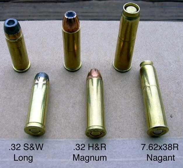 Three revolver cartridges standing upright and lying flat: .32 S&W Long and .32 H&R Magnum with visible lead or jacketed bullet noses, and a 7.62x38R Nagant whose case mouth is crimped shut over a bullet seated entirely inside the case