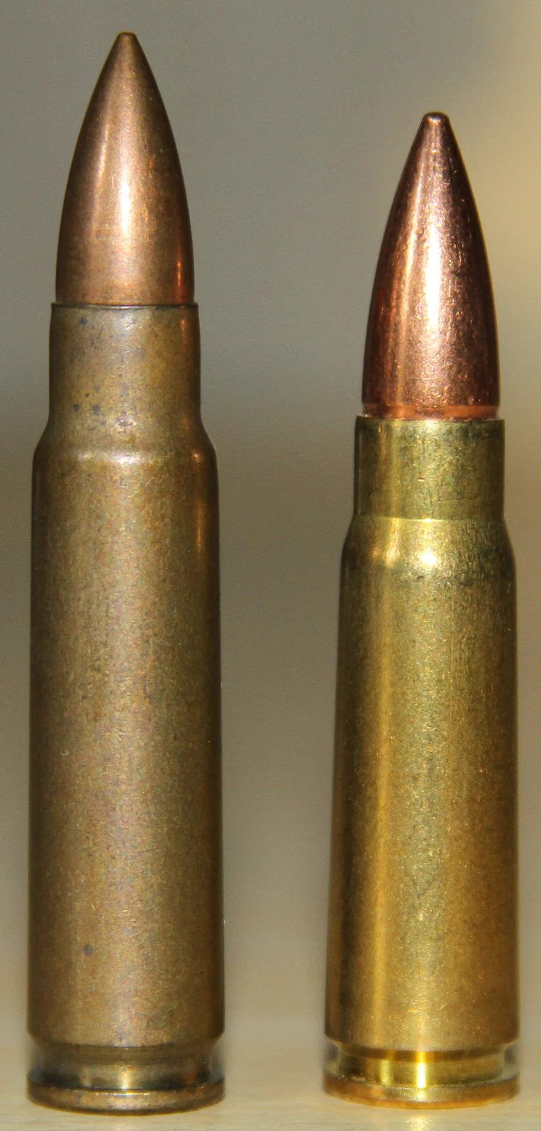 Two brass bottleneck rifle cartridges standing side by side, the left one visibly longer
