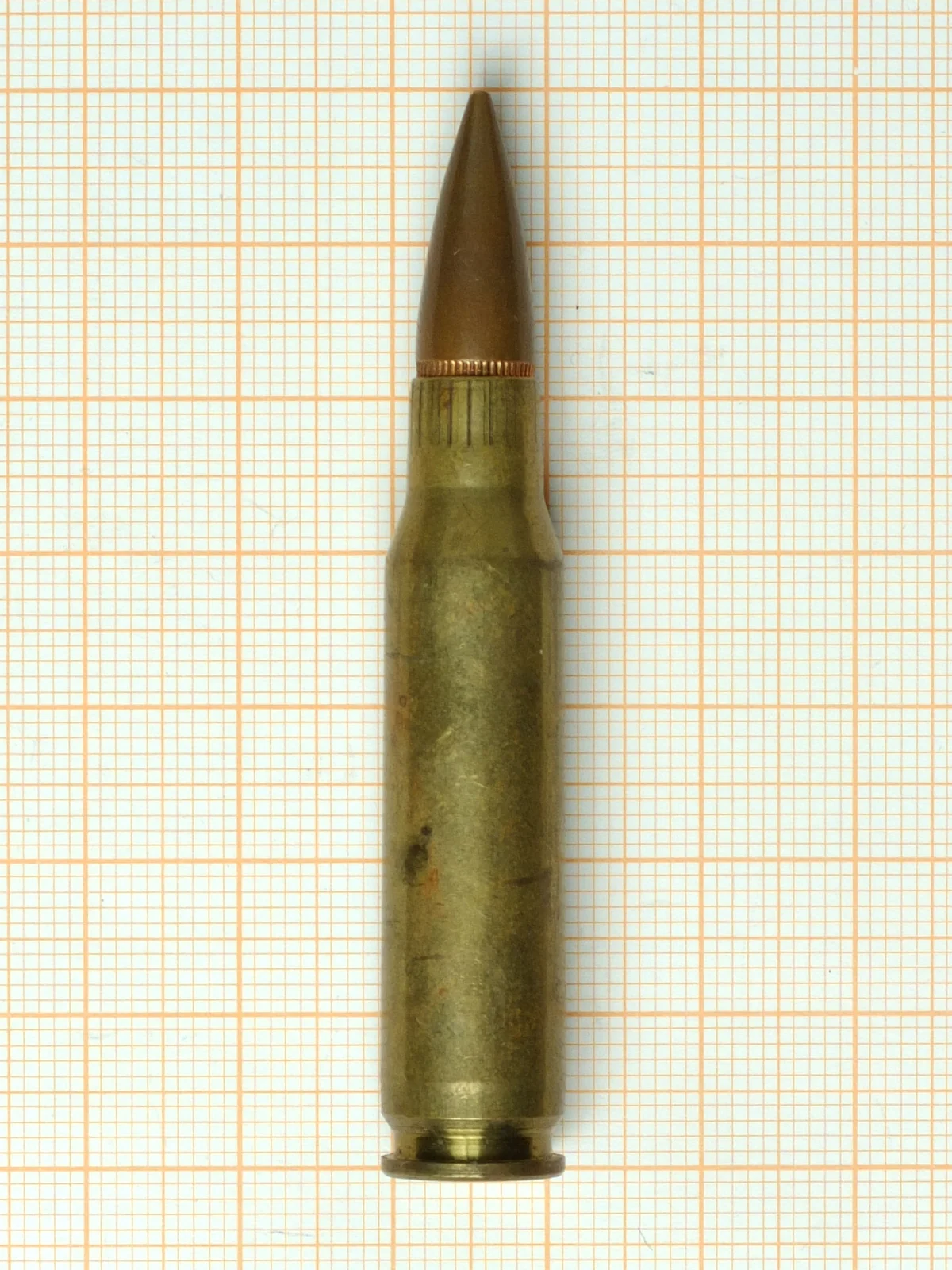 A 7.62×51mm NATO cartridge on orange graph paper, bottlenecked with a long pointed full metal jacket bullet.