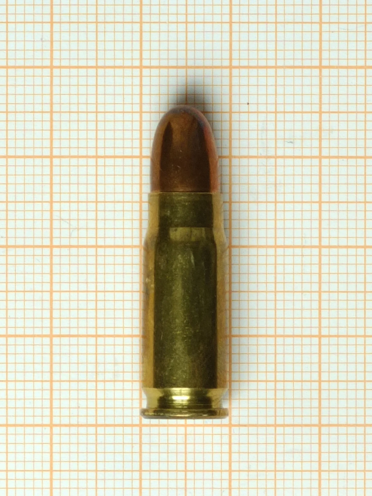 A bottleneck rifle-length pistol cartridge with a rounded copper-jacketed bullet, photographed on graph paper.