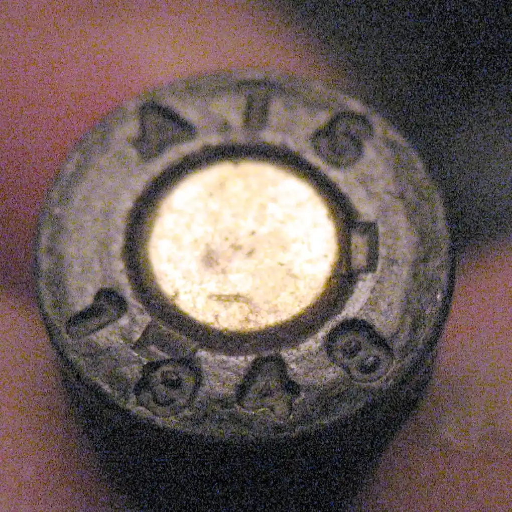 Close-up of a 7.65mm Longue cartridge base, stamped with the letters ATS and the year 1948 around the primer