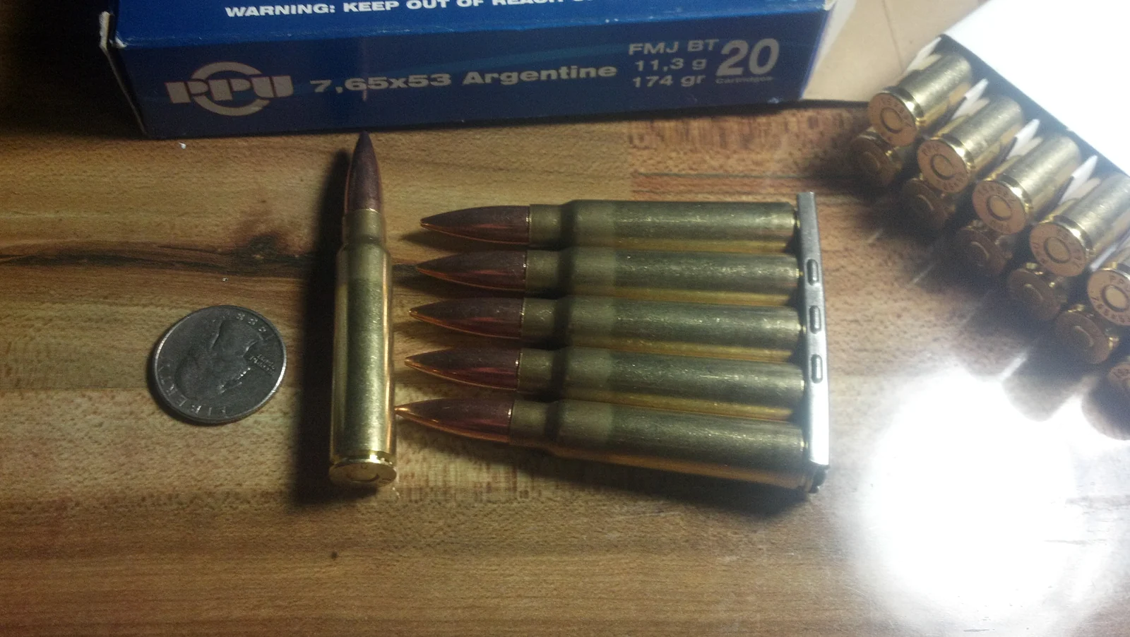 A row of six 7.65x53mm Argentine cartridges with brass cases and pointed bullets, leaning against an ammunition box printed with the caliber
