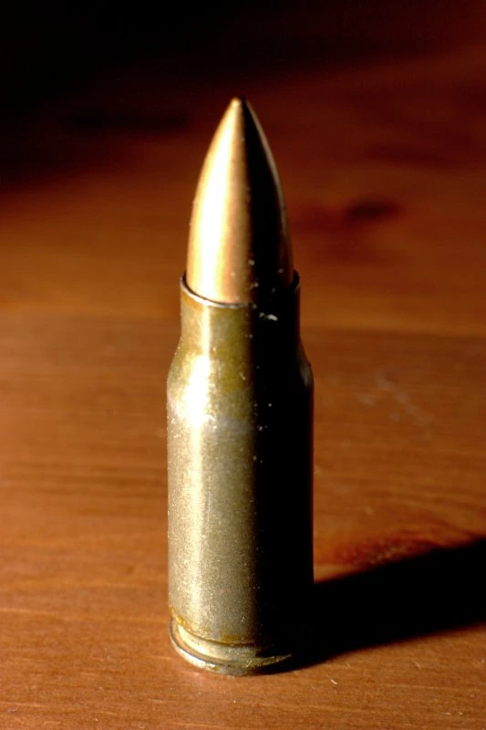 A 7.92×33mm Kurz cartridge standing on a wooden surface in warm light, noticeably short for the width of its case.