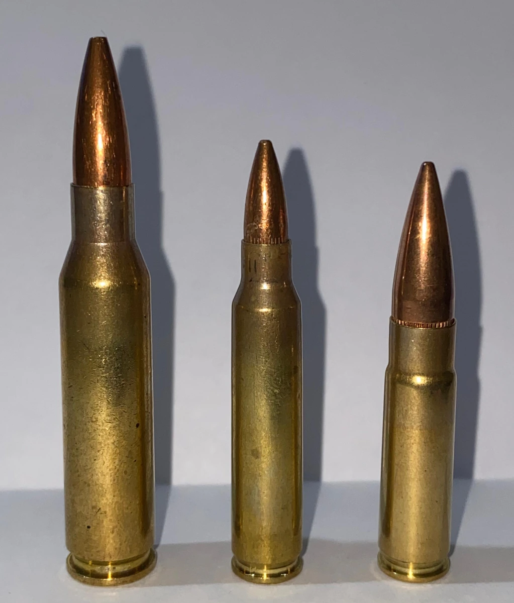 Three brass rifle cartridges of different sizes standing side by side against a grey background: a tall one on the left with a long pointed bullet, a slightly shorter and narrower one in the centre, and a shorter, stockier one on the right with its bullet seated deep in the case.
