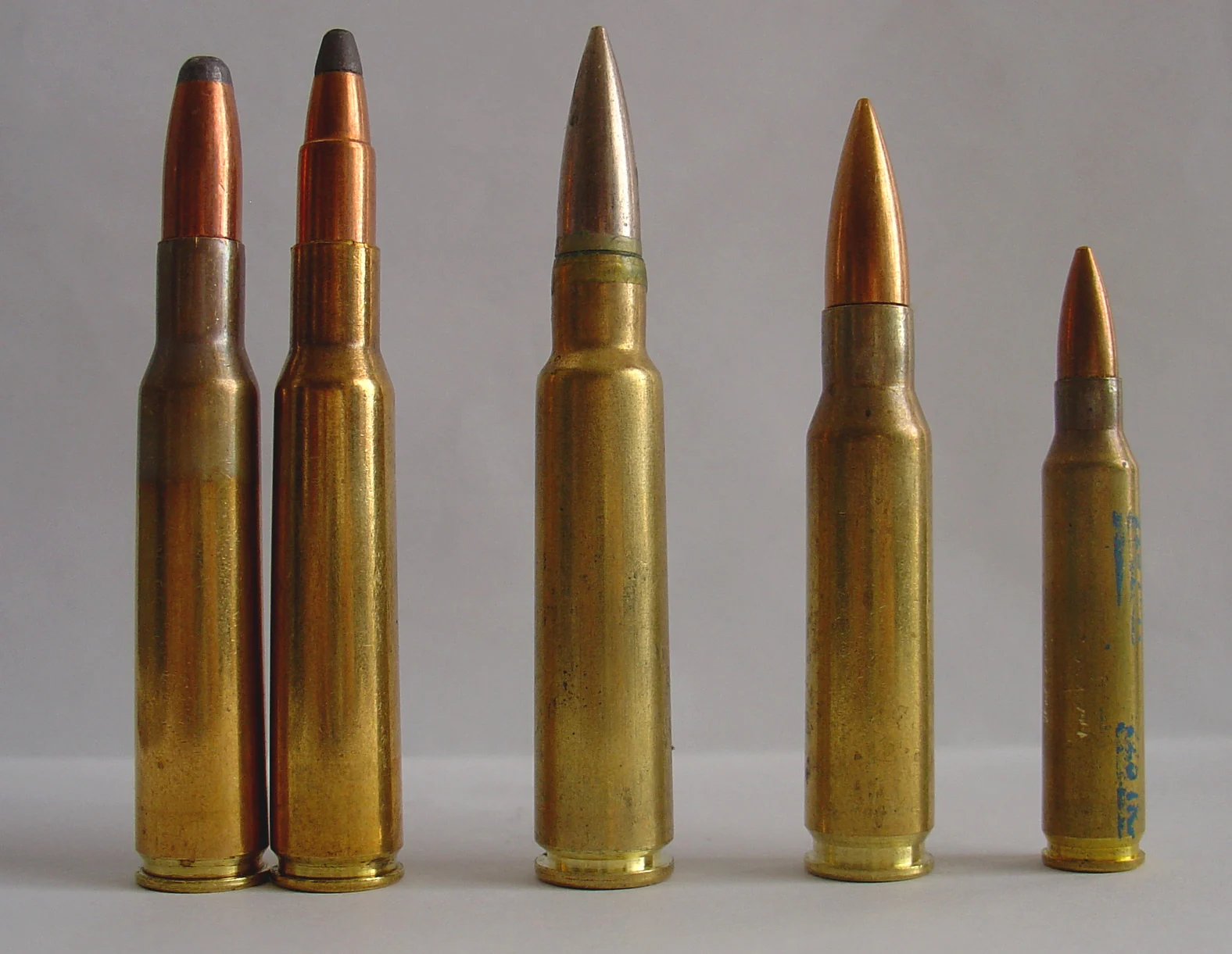 Five rifle cartridges standing upright for size comparison: two 7×57mm Mauser rounds with soft-point bullets on the left, a 7.5×55mm Swiss GP11 in the centre, a .308 Winchester, and a smaller .223 Remington on the right